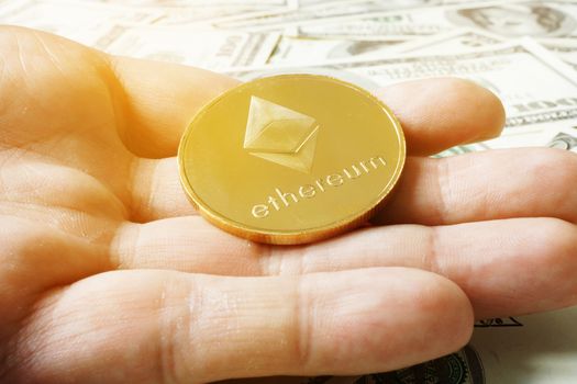 Hand is holding coin ethereum ETH under dollar banknotes. Cryptocurrency mining.