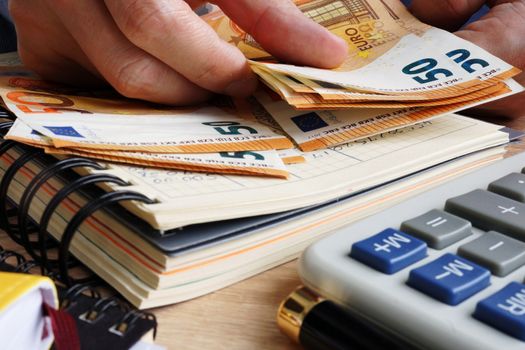 Man counting euro banknotes. Desk with calculator, ledger and euros.