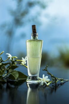 Close up of spray or perfume of Indian jasmine flower or juhi or Jasminum Auriculatum on wooden surface in a small bottle with raw flowers.