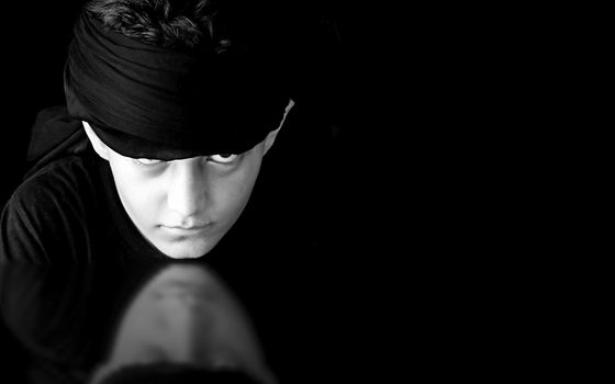 Portrait shot of a young male Caucasian model wearing black colored cloth at the head and its shadow isolated on black.Low key portraits.