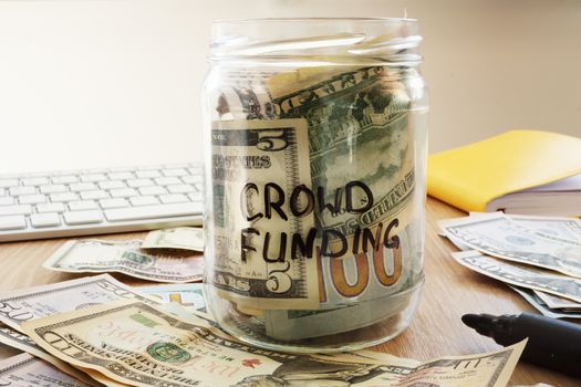 Crowdfunding written on a jar with dollars.