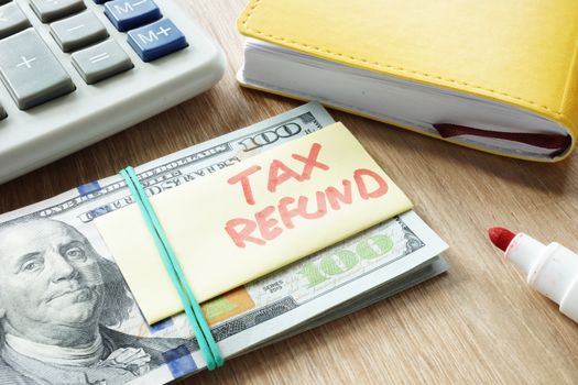 Tax refund written on a memo stick and dollar bills.