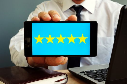 Man holding smartphone with five stars rating. Customer satisfaction.