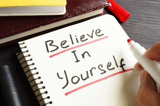 Man is writing Believe In Yourself in a note. Motivation.