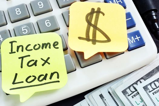 Income Tax Loan written on a stick. Calculator and cash.