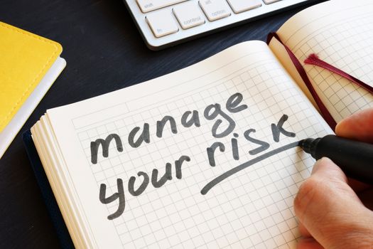 Man is writing manage your risk in a note.