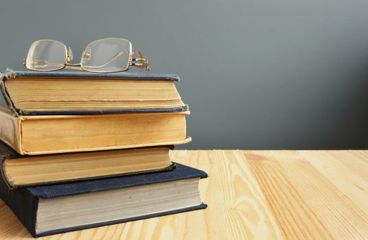 Retro books and old eyeglasses on wooden table.