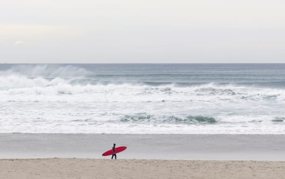 Red board surfer walking on the beach with waves in the background