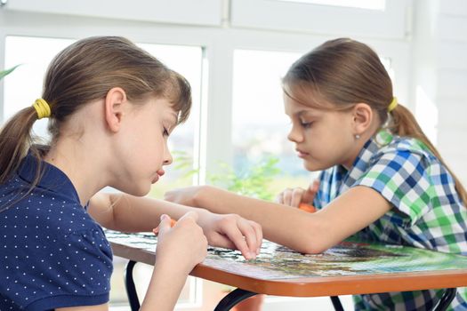 Two girls enthusiastically collect puzzles at the table at home