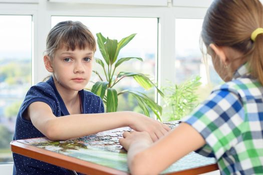 Sad girl collects puzzles in the company of girlfriends and looked into the frame