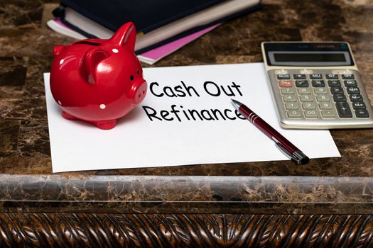 Paper with the words cash out refinancing on a marble table next to a red piggy Bank.