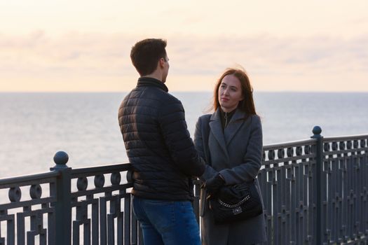 Girl anxiously looks at a guy near a railing in the background of the sea in cloudy weather