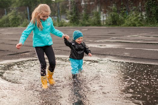 Boy and girl jumping in puddle in waterproof coat and rubber boots