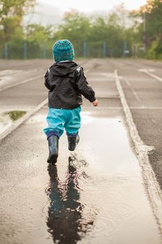 Child jumping in puddle in waterproof coat and rubber boots