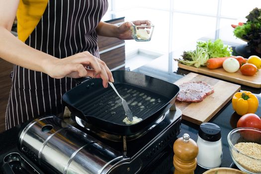 The housewife dressed in an apron putting butter in the pan prepared for frying steaks.