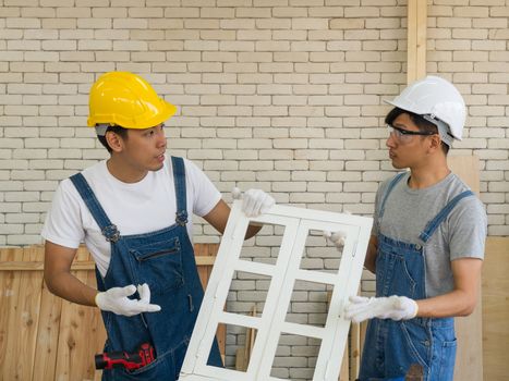 Two Asian carpenters argued about the faults of the newly assembled windows. Handyman wearing a hard hat, Fabric gloves with a trusted drill In the morning work atmosphere