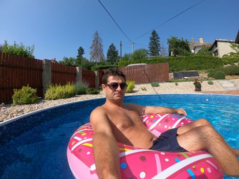 Happy man relax on inflatable ring in small home swimming pool. Covid 19, Summer Holiday 2020 holiday concept. Vacation at home or on garden.