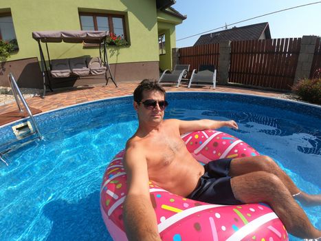 Happy man relax on inflatable ring in small home swimming pool. Covid 19, Summer Holiday 2020 holiday concept. Vacation at home or on garden.