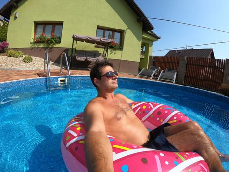 Happy man relax on inflatable ring in small home swimming pool. Covid 19, Summer Holiday 2020 holiday concept. Vacation at home or on garden.