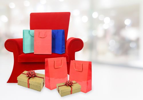 Composite image of a red armchair of Santa Claus with Christmas gifts and copy space on the background of a blurred shopping mall interior.