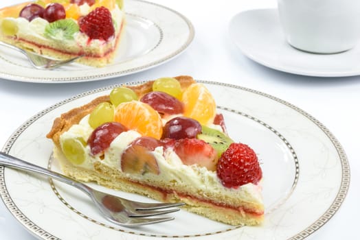 Conception of healthy fruit dessert - fresh homemade multi fruit tart on plates with cup of coffee in close-up.