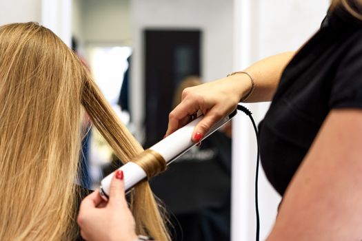 Professional services in the beauty salon - a young woman with beautiful blond hair has made hairstyles with a curling iron.