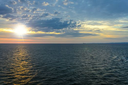 Picturesque sea landscape - the sun rises over the sea against a cloudy sky and in the distance you can see the ship and land.