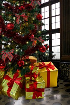 Composite image of luxury gifts with red ribbons under a richly decorated Christmas tree on a historical interior background.