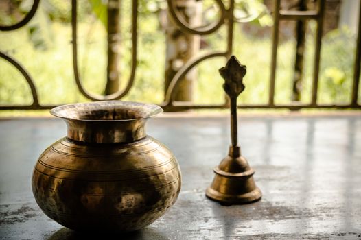 Close up Still Life of antique Holi water pot and bell on rustic floor. Faith, Tradition, Spirituality, Prayer, symbols of peace and Religious Themes. Arts and culture background concept. Copy space room for text for massage.