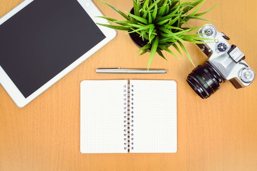 Concept of creative workplace - top view of retro slr camera, green flower, digital tablet and notepad with pen on a wooden desk. 