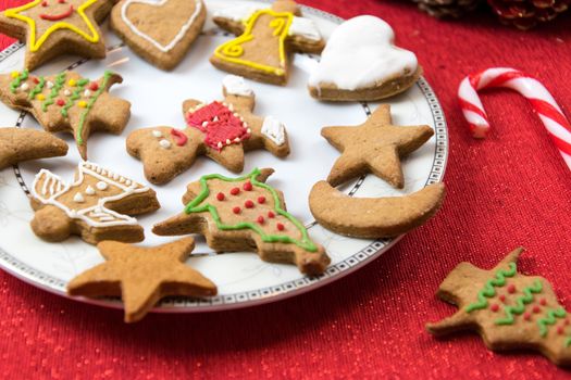 Concept image of Christmas fun with children - a variety of homemade gingerbreads on a red tablecloth in close-up.