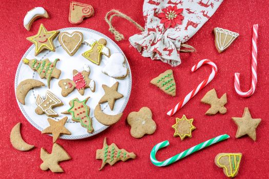 A conceptual image of Christmas fun with children - a variety of homemade gingerbreads on a red tablecloth with decorations. 