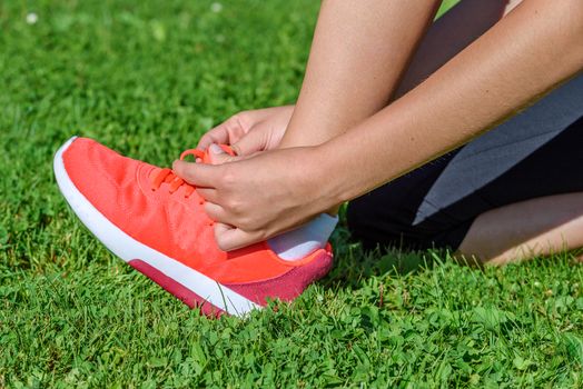 Runner woman kneeling on the grass and tying shoelaces on a sunny day