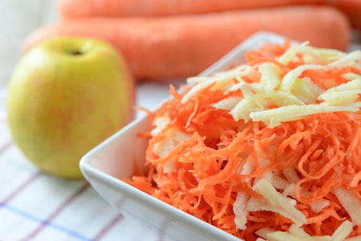 Healthy salad concept - grated carrot with apple in a white platter in close-up