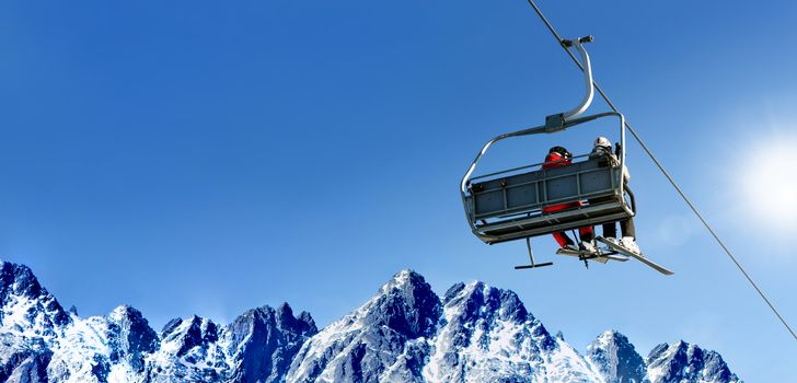 Composite image of skiers on a ski lift in high mountains on the background of a clear blue sky with large copy space.