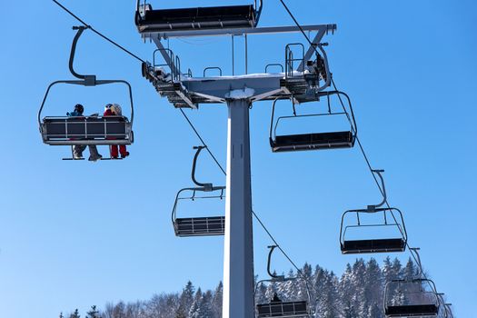 Skiers on a ski lift in the mountain on the background of a clear blue sky