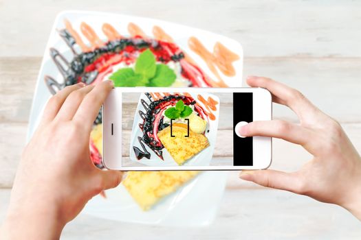 Composite image of making culinary photo on a smartphone - woman's hands holding mobile phone and touching shutter button on the screen.