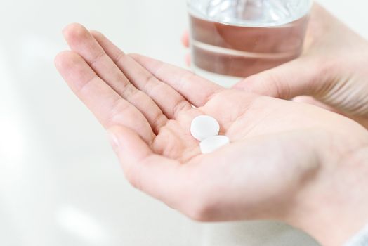 Concept image of treatment  - hands of young woman with pills and water in close-up.