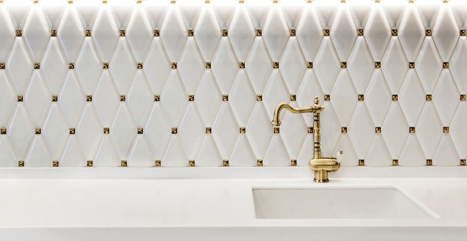 Fragment of a modern kitchen. Sink with faucet made of bronze on a white glossy kitchen worktop.