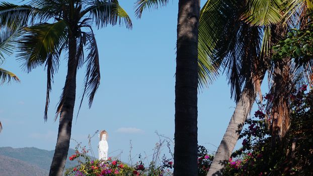 Sanya, Hainan, China - Landscape with tropical palm trees and Goddess of Mercy located in the sea against blue sky in Nanshan Buddhist Cultural Centre