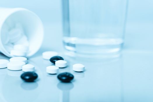 Pharmaceutical  treatment background - groups of pills and glass of water in close-up (blue filter effect)