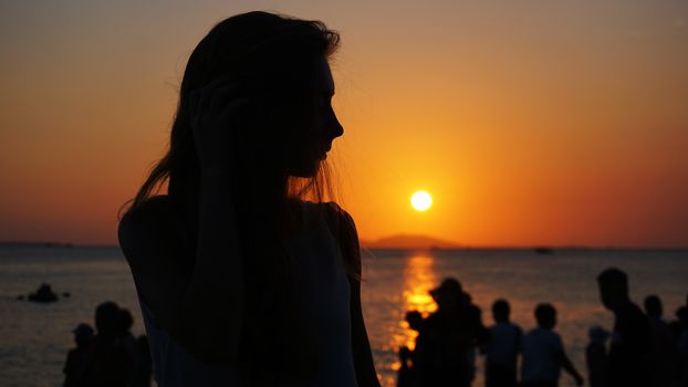 Side view of back light of a woman silhouette warm sunset in front of sun - tourist beach at sunset