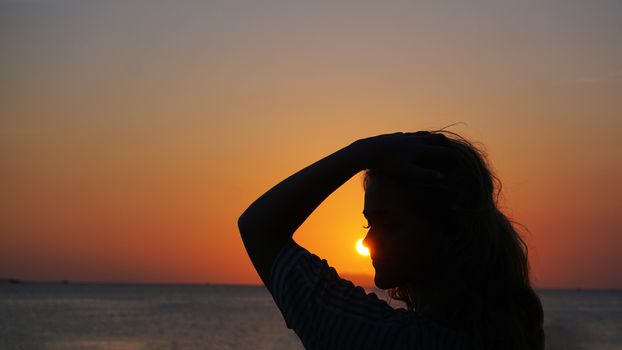 Side view of back light of a woman silhouette warm sunset in front of sun - tourist beach at sunset