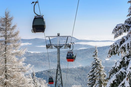 Gondola cabin lift in the ski resort over the forest on the background of snowy mountains in sunny day (high details)