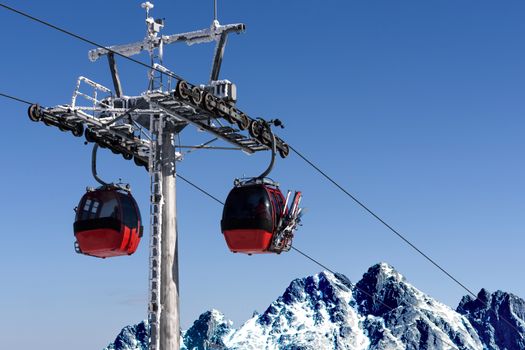 Gondola cabin lift in the ski resort over the high mountains on the blue sky background in sunny day with copy space.