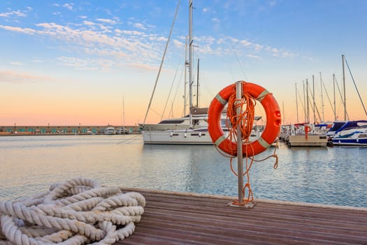 a mooring rope with a lifebelt  on  the quay of a marina at  the sunset