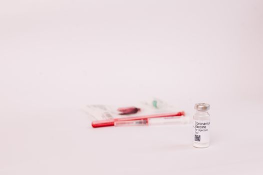 Coronavirus vaccine. Medical preparation in ampoule. Treatment for the disease, covid-19. The vaccine on a white background and on the background of a syringe, rubber gloves and goggles.