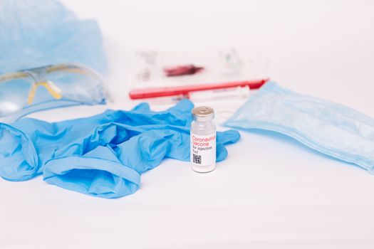 Coronavirus vaccine. Medical preparation in ampoule. Treatment for the disease, covid-19. The vaccine on a white background and on the background of a syringe, rubber gloves and goggles.