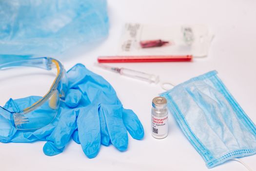 Coronavirus vaccine. Medical preparation in ampoule. Treatment for the disease, covid-19. The vaccine on a white background and on the background of a syringe, rubber gloves and goggles.