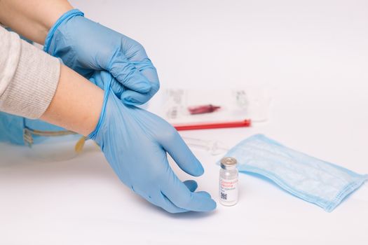 Coronavirus vaccine. Medical preparation in ampoule. Treatment for the disease, covid-19. The vaccine on a white background and on the background of a syringe, rubber gloves and goggles.